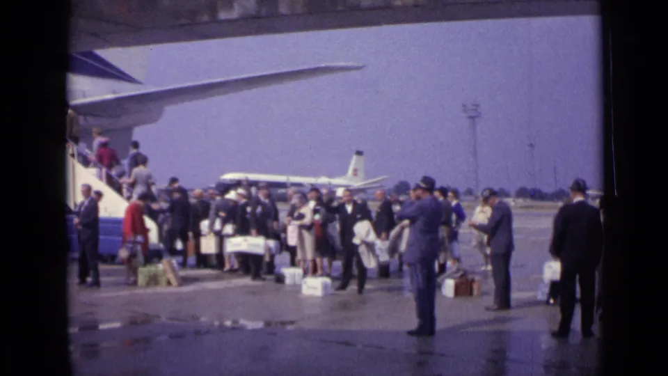 1962 London tarmac boarding scene with passengers, luggage, mobile stairs, and a jet airliner visible in the background.