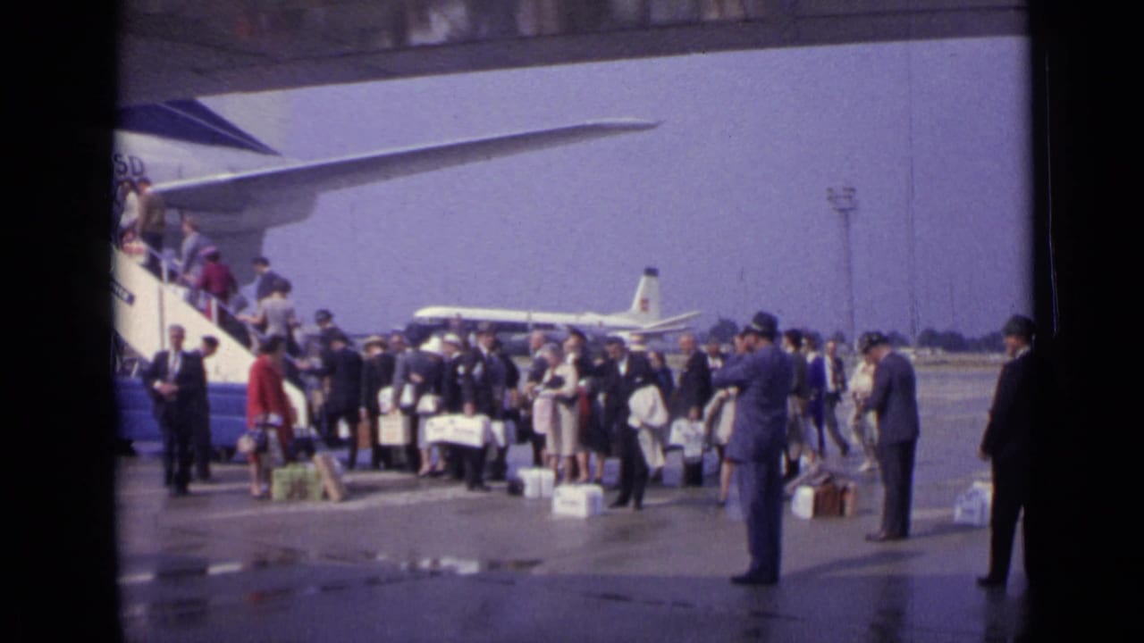 Passengers wait on a wet tarmac near boarding stairs and a Boeing 707 wing.