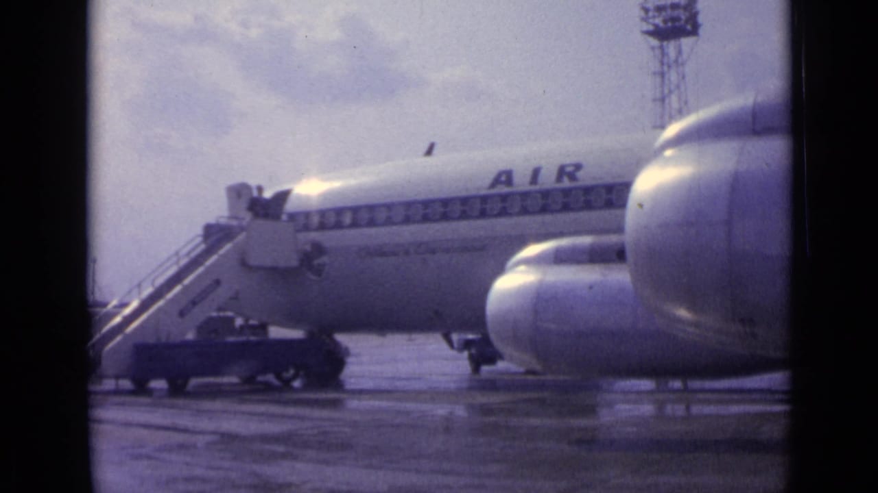 Passenger jet on wet tarmac with mobile stairs and partial blue lettering visible.