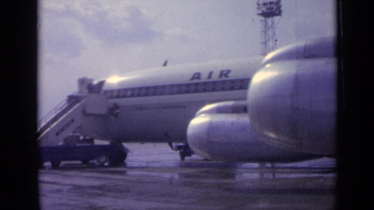 Jet fuselage and large foreground engine area seen across a wet airport apron.