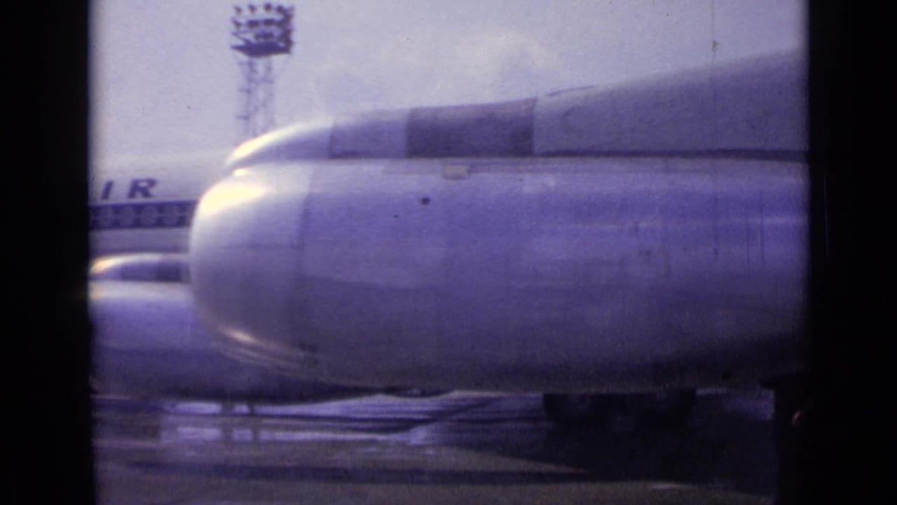 At the end of the pan, a large engine nacelle fills the foreground while partial airline lettering and the wet apron remain visible.