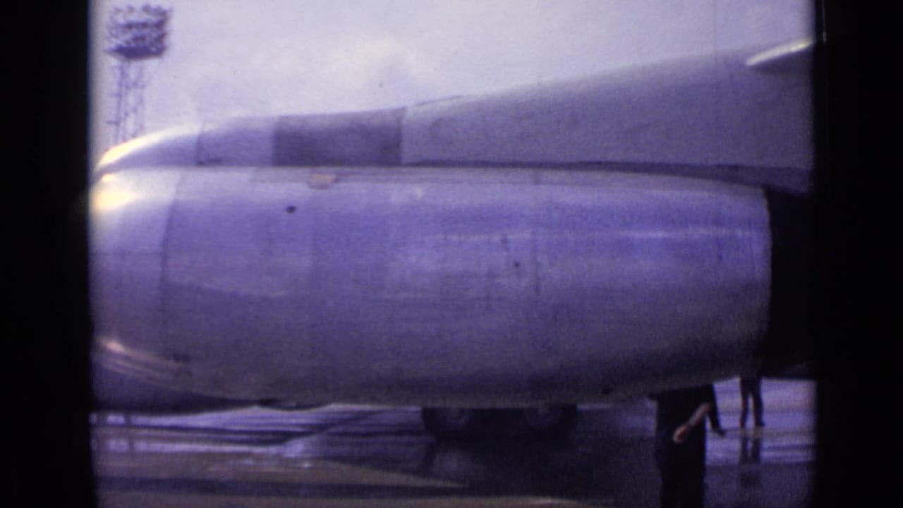 Boeing 707 engine and wing over wet airport tarmac with ground crew nearby.