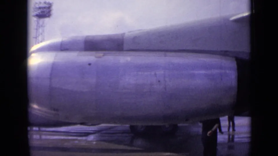1962 London airport footage showing a close view of a Boeing 707 engine, wing underside, and wet tarmac with staff partly visible.