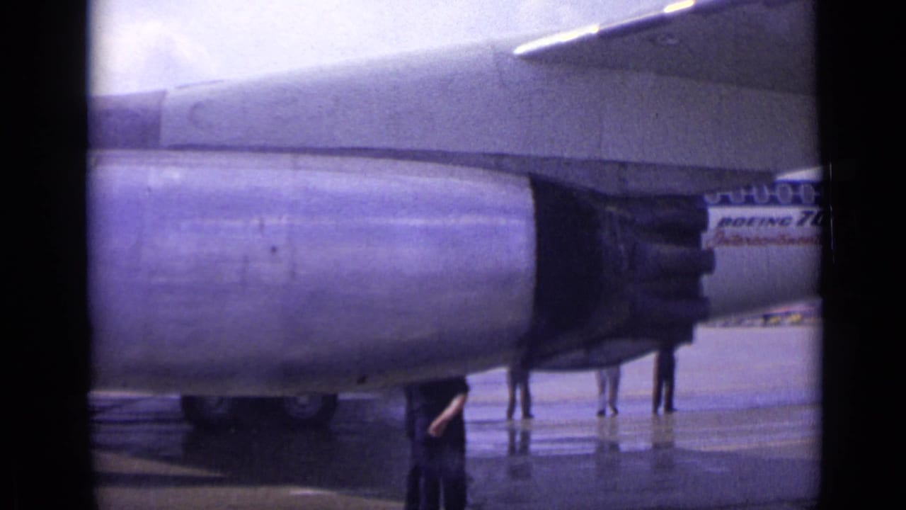 A Boeing 707 engine fills the frame at a London airport in 1962, with the aircraft fuselage and tarmac figures visible behind it.