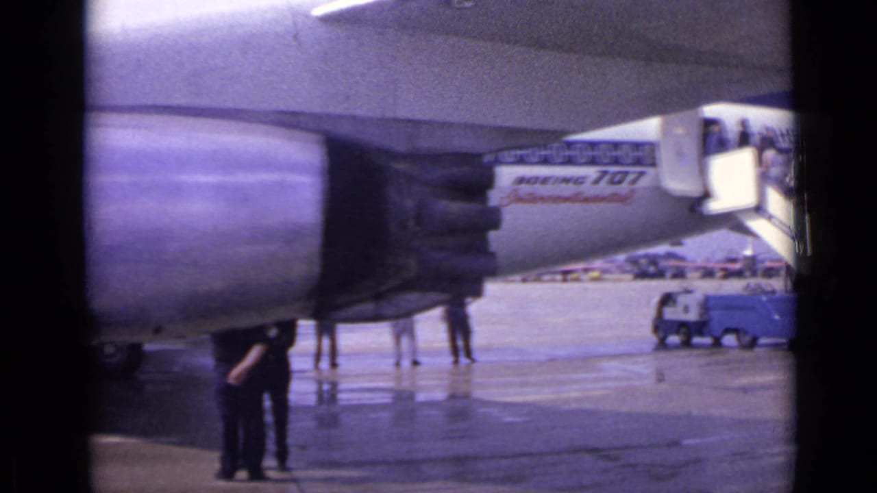 1962 London airport footage showing a jet engine, mobile stairs, wet tarmac, and passengers near a Boeing 707 Intercontinental.