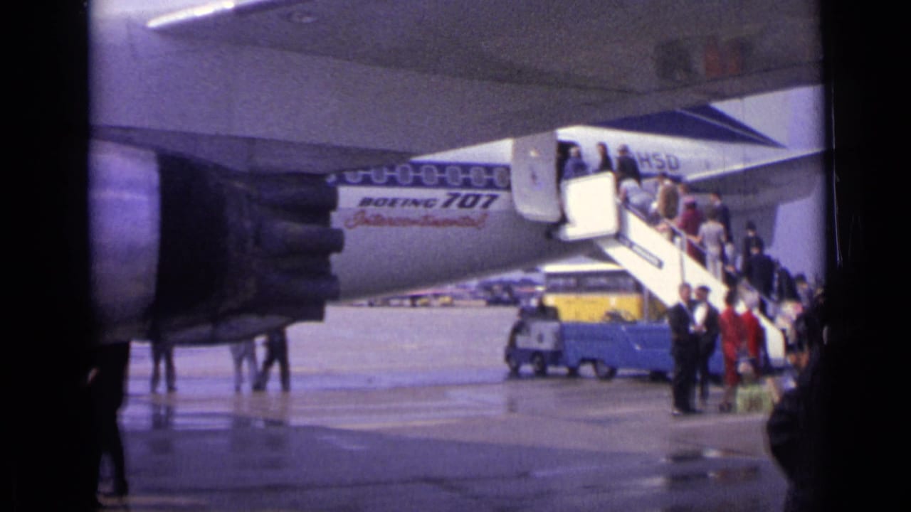 Passengers descend or queue on mobile stairs beside a Boeing 707 on the tarmac.