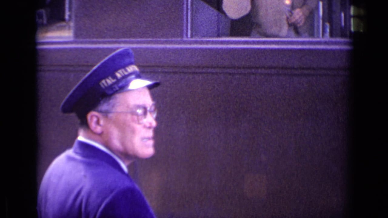 Uniformed man in blue cap walking beside a train carriage.