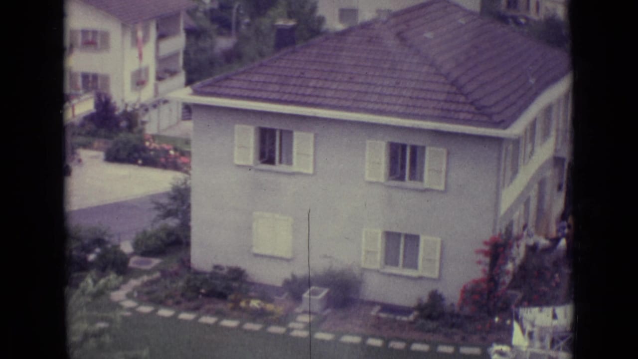 White house with pale shutters, tiled roof, garden paths, and surrounding greenery.