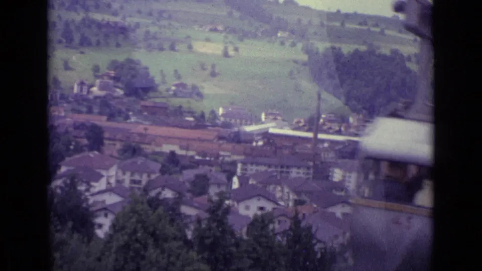 1962 Lucerne cable-car view with hillside fields, clustered houses, trees, and valley buildings framed by dark gondola structure.