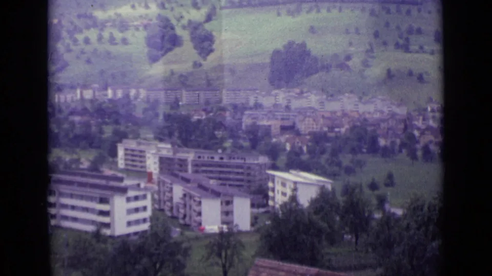 1962 Lucerne cable-car still showing apartment buildings, rooftops, green fields, trees, and dark gondola framing.