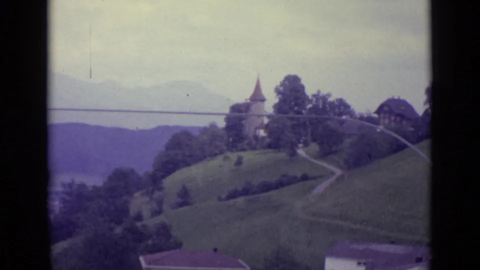 1962 Lucerne-area hillside view with a church tower, trees, a curving path, and hazy distant landscape beyond.