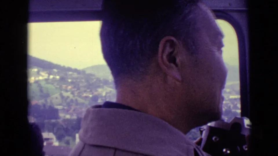 1962 Swiss travel footage shows an adult man in profile looking out from a moving vehicle toward Lucerne-area hills and buildings.
