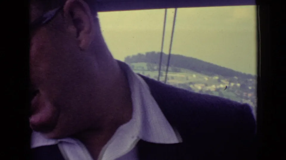 A man in glasses and a dark jacket sits by a cable car window during a 1962 Swiss mountain ride.