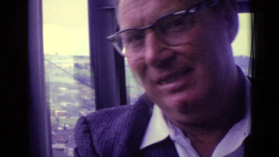 A smiling man in glasses is framed by the cable car interior, with Swiss hillside scenery visible outside.