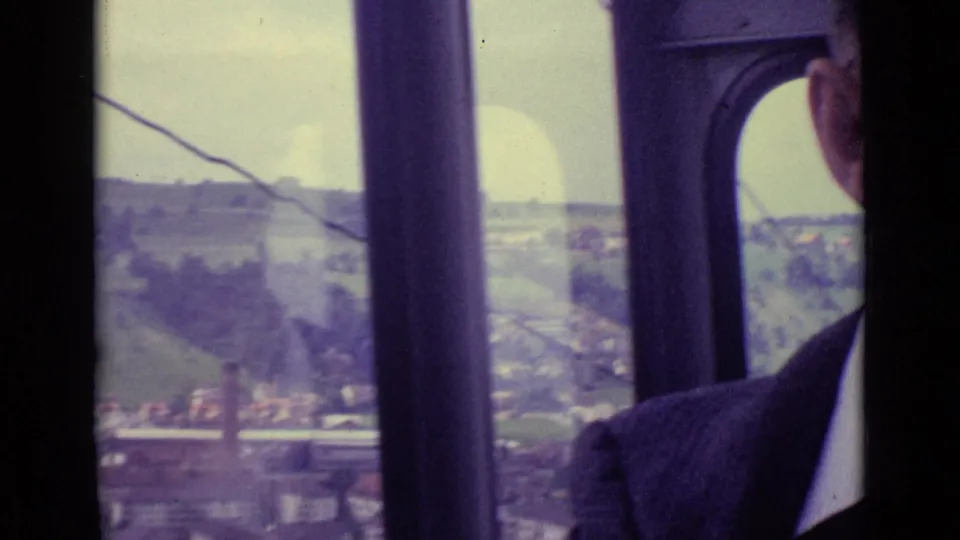 The cable car window shows a moving view over hills and village rooftops near Lucerne, with a passenger partly visible.