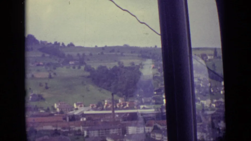 Lucerne-area hills and scattered buildings in 1962, partially blocked by cable-car window supports and reflections.