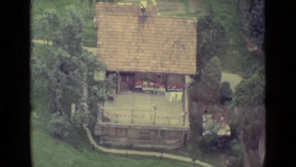 Overhead 1962 Swiss countryside view of a tiled-roof house, garden area, trees, and paths from a cable car.
