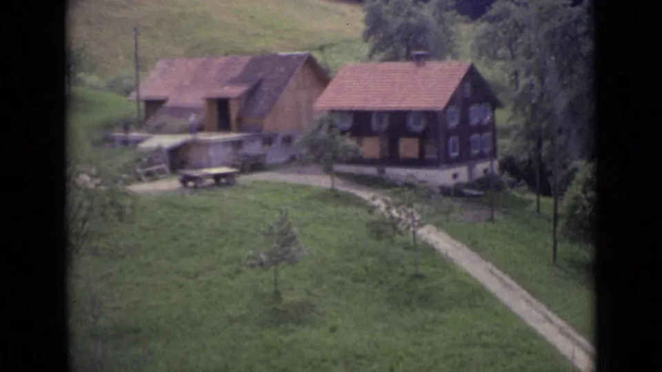 Lucerne-area home-movie view of chalet-like houses, red roofs, a footpath, and green hillside pasture in 1962 footage.