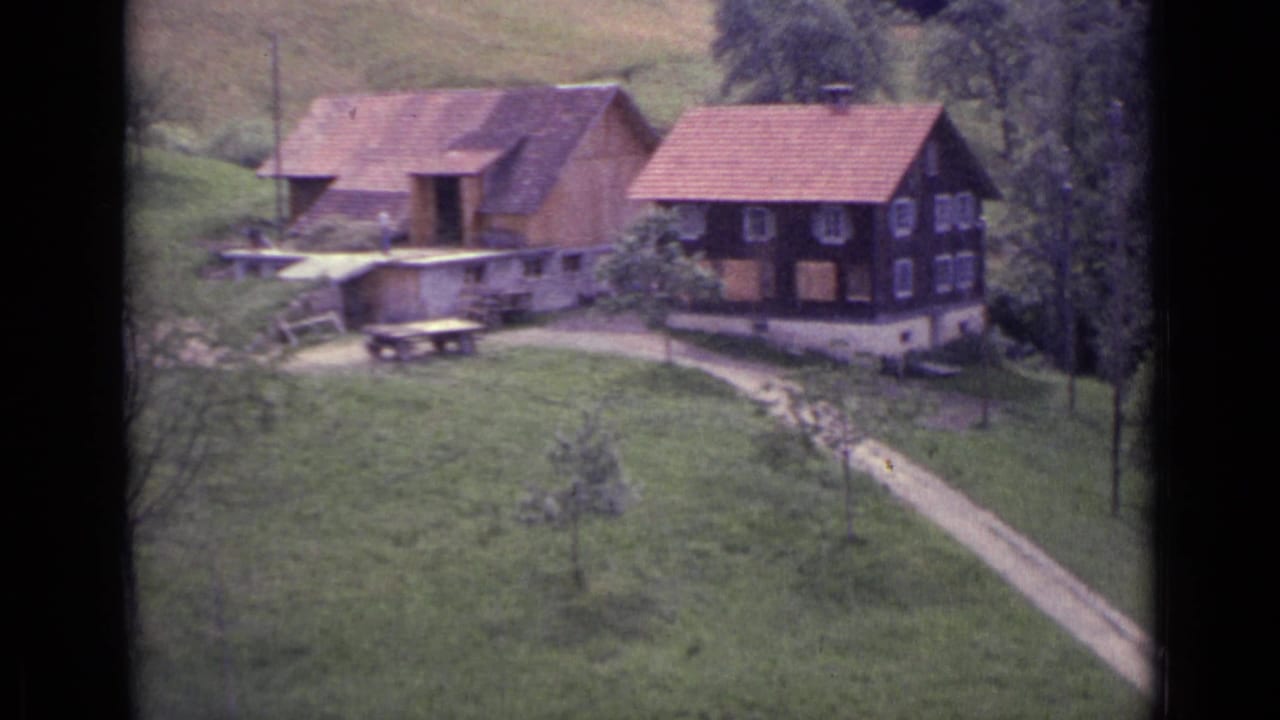 Two timber houses with red-tiled roofs on a green hillside beside a winding dirt path.