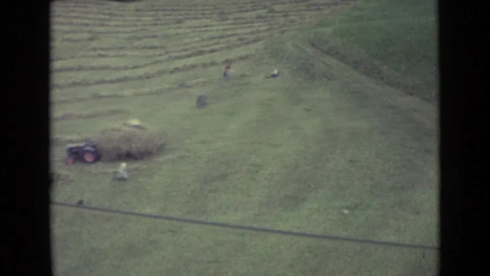 End frame from the Lucerne 1962 home movie, with workers and a small tractor visible across a harvested hillside field.