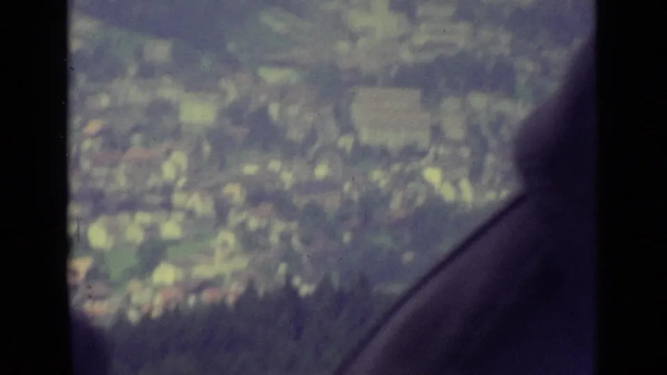 Aerial view over Lucerne from a moving cable car, with window framing and a dark edge partly covering the city below.