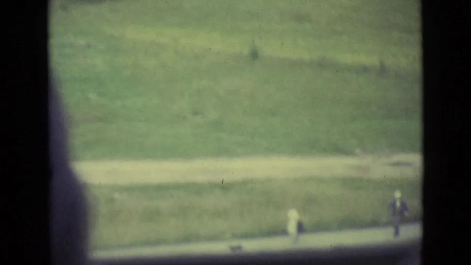 Downward 1962 Lucerne view of a grassy field and walkway with distant, indistinct pedestrians.