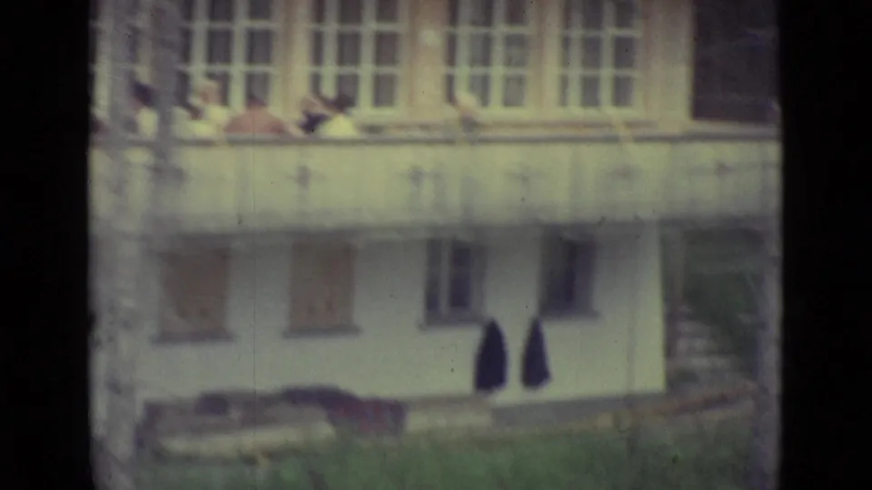 Lucerne 1962 frame of the white building exterior, with balcony activity above and dark garments hanging near the lower level.