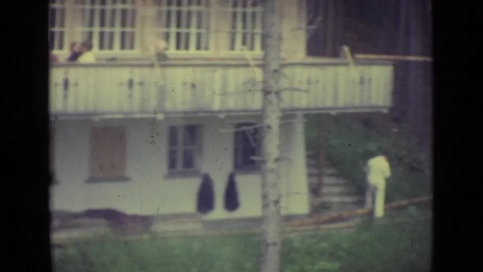 1962 Lucerne frame showing the white building, balcony, leaning ladder, and a person in light clothing near the lower steps.