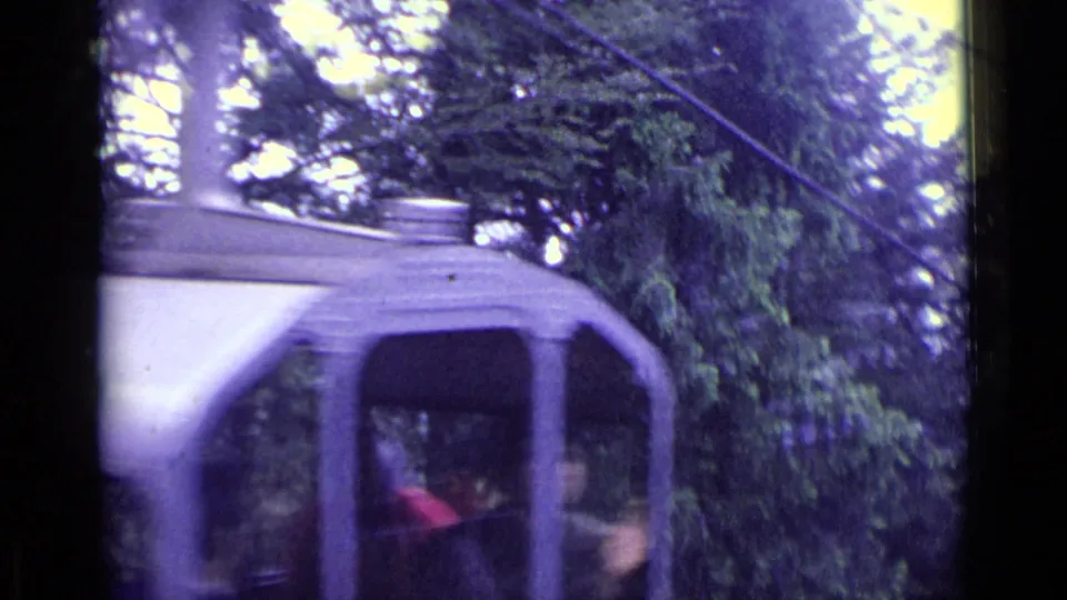 An enclosed gondola moves past dense trees in the 1962 Lucerne cable car footage, with passengers faintly visible.