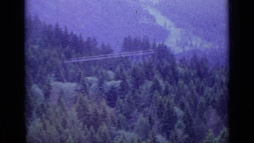 Cable wires cross a wooded Swiss mountainside in the Lucerne 1962 home-movie footage, with distant hills in soft focus.