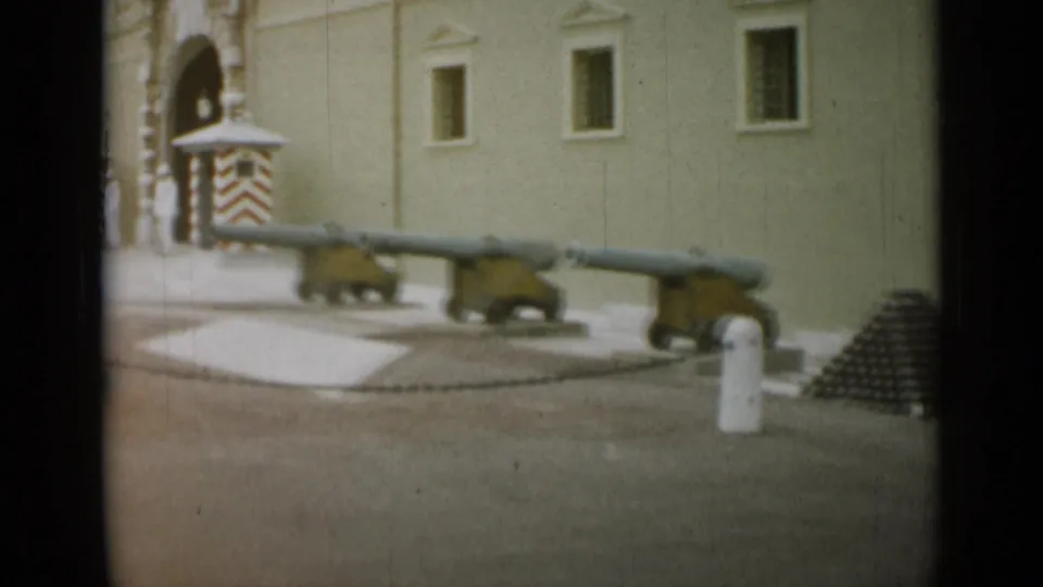 1962 Monaco 8mm frame with displayed cannons, cannonball stacks, a striped sentry box, and an arched entrance near a pale facade.