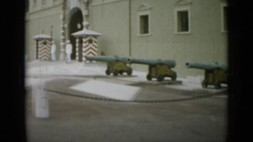 1962 Monaco home-movie frame showing cannon barrels, a palace wall, a striped sentry box, and a guard near an arched entrance.
