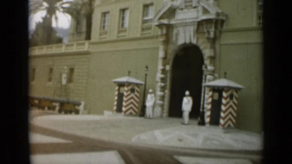1962 Monaco footage showing white-uniformed guards by a grand arched building entrance with striped sentry boxes.