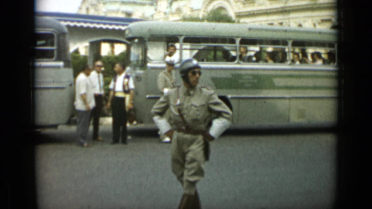 Uniformed man in helmet stands before a light-colored bus on a city street.
