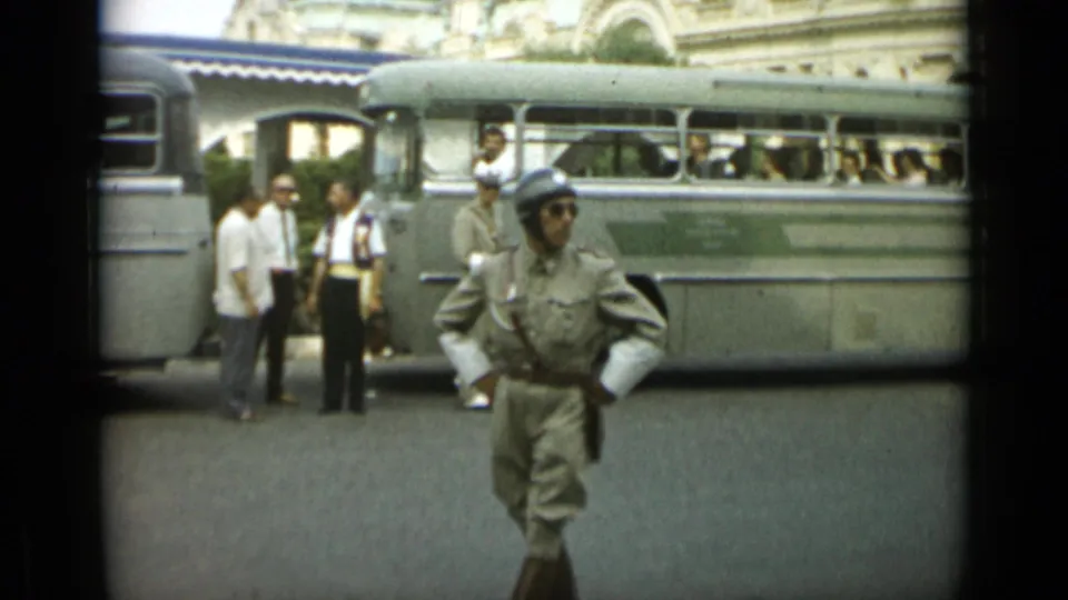 In Monaco, 1962, a helmeted uniformed man faces the camera while a light-colored bus and several men stand behind him.