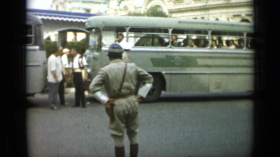 In Monaco, 1962, the uniformed man has turned away from the camera toward a large light-colored bus with passengers visible.