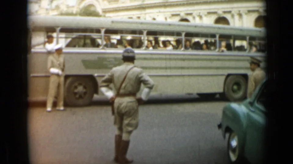 In Monaco, 1962, the uniformed man stands with a bus behind him and a green vintage car partly visible at the right edge.