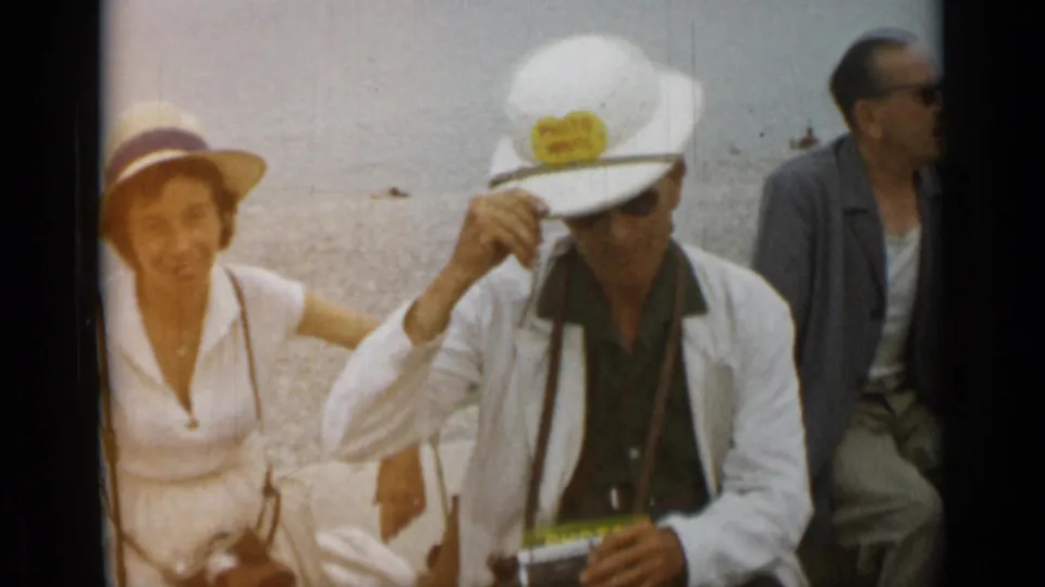 1962 Monaco waterfront frame showing seated visitors in sun hats and sunglasses beside the water.