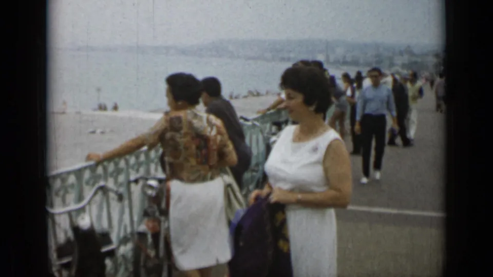 1962 Monaco promenade view with pedestrians, two women near a railing, a bicycle, and water in the background.