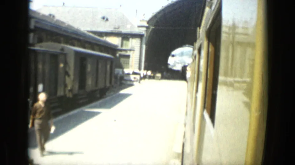 1962 Monaco travel frame showing a train station platform, train side, station buildings, and an arched roof structure.