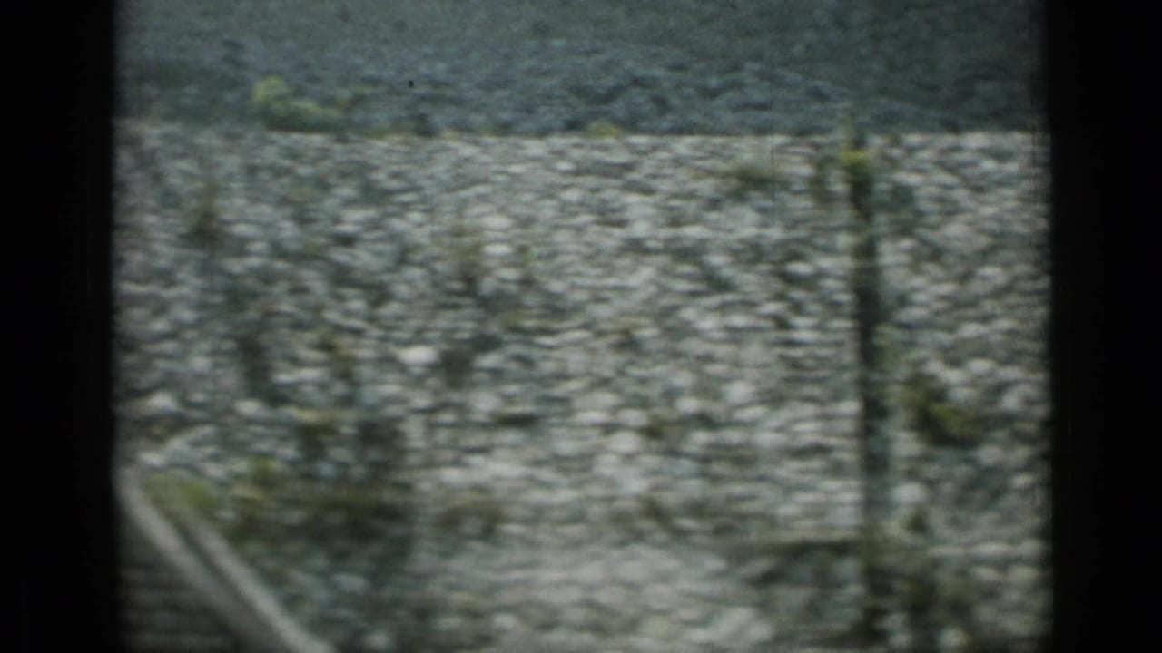 1962 Monaco home-movie frame showing a motion-blurred cobblestone surface with dark film edge and roadside vegetation.