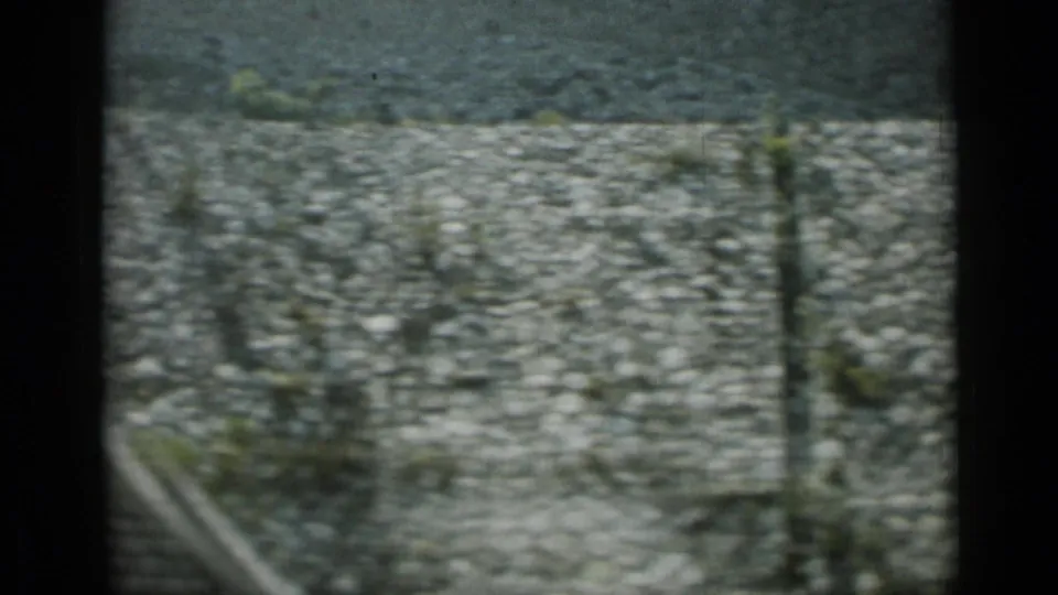 1962 Monaco home-movie frame showing a motion-blurred cobblestone surface with dark film edge and roadside vegetation.