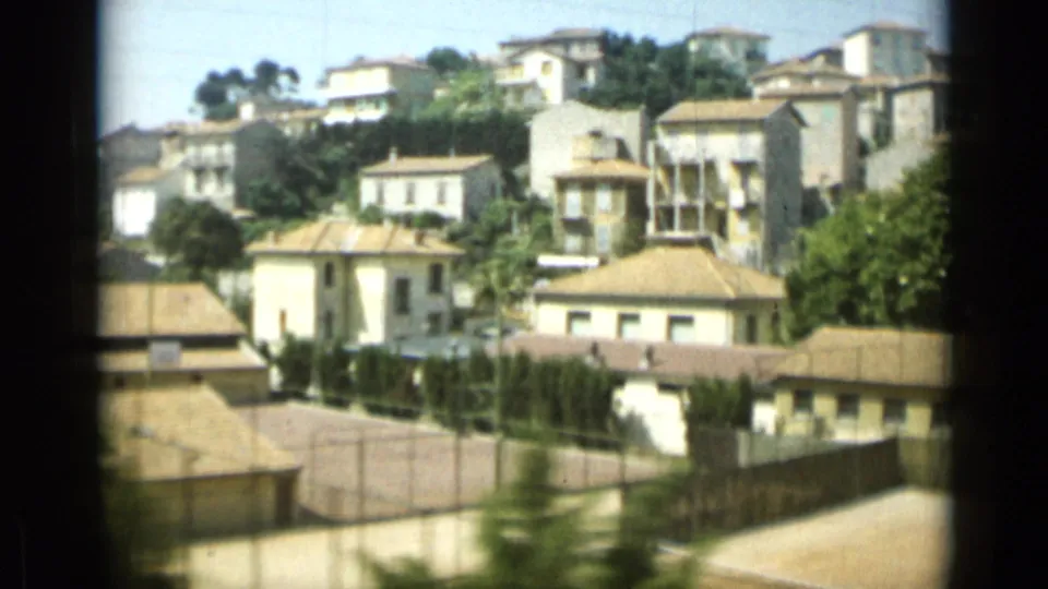 1962 Monaco view of hillside residential buildings, tiled roofs, trees, and a wall, partly obscured by the film frame edge.