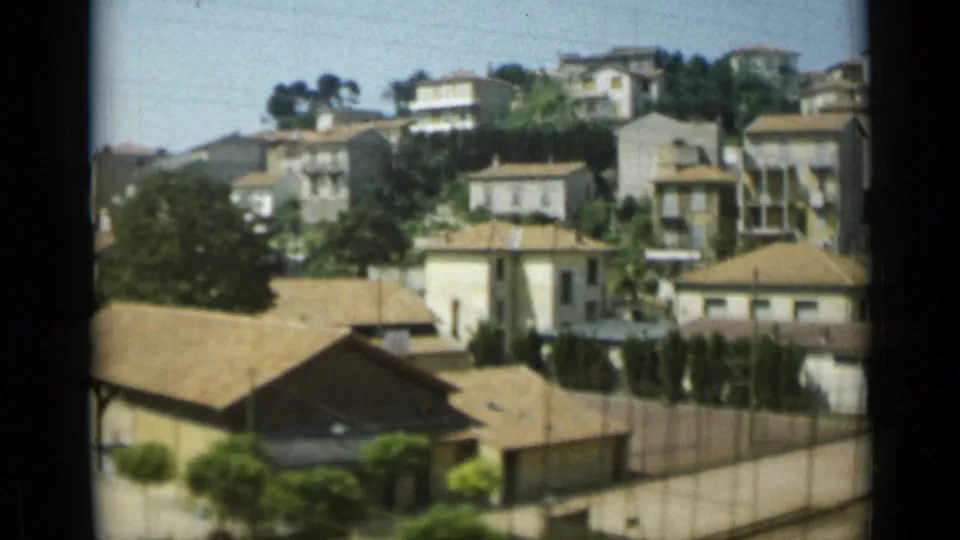 1962 Monaco home-movie frame showing clustered hillside homes, terracotta roofs, greenery, and a walled street edge.