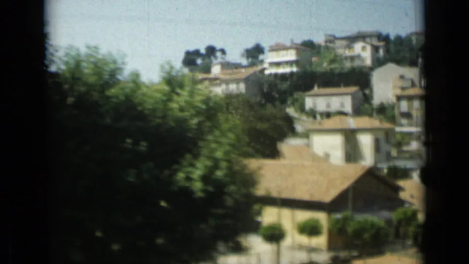1962 Monaco moving-view frame with hillside residences, tiled roofs, a street edge, and blurred foreground foliage.