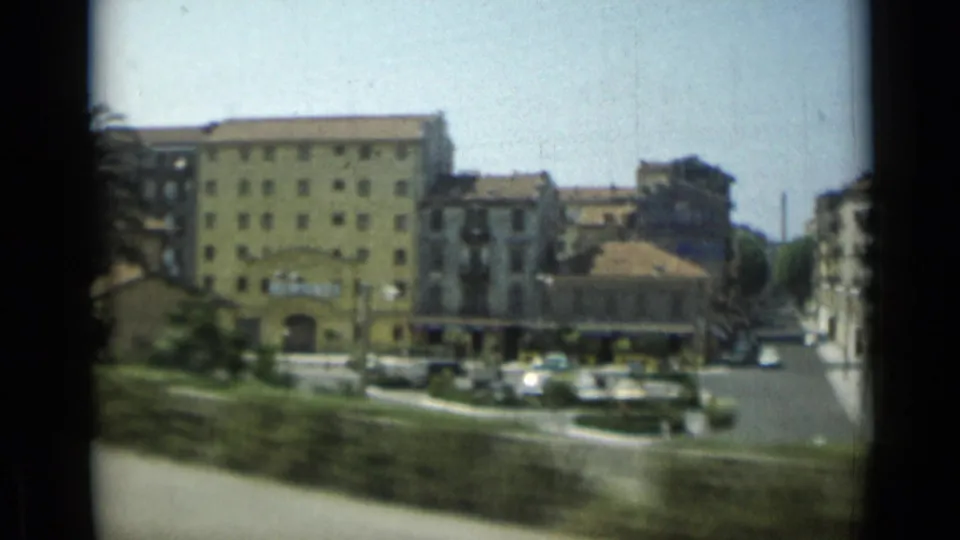 1962 Monaco travel footage showing a yellow apartment block, nearby street traffic, trees, and urban buildings from a moving vehicle.