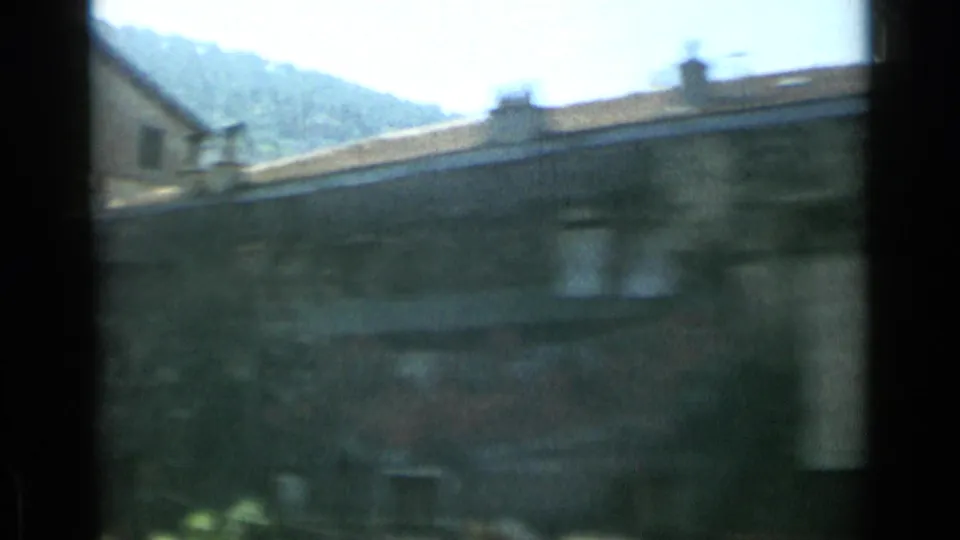 Soft 8mm Monaco city view with rooflines, hillside backdrop, and dark film or window edge crossing the frame.