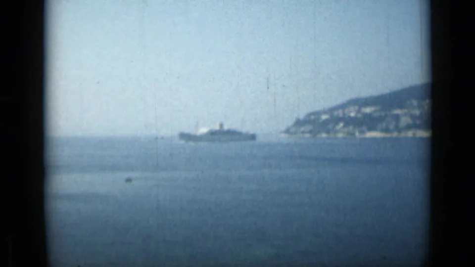 1962 Monaco coastal frame showing a large ship offshore, calm Mediterranean water, and a distant built-up hillside.