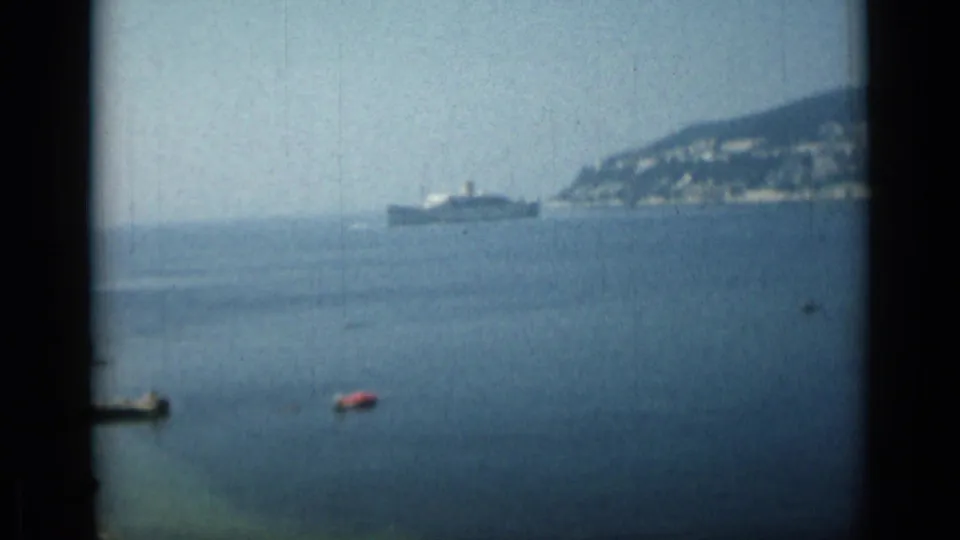 1962 Monaco harbor footage showing blue water, a distant ship near the coast, small boats, and dark edges from the moving viewpoint.