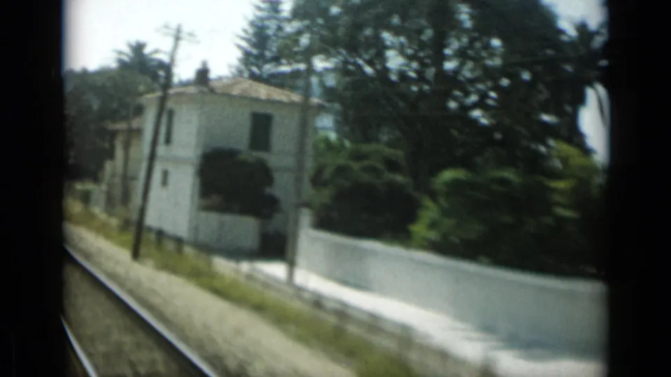 A white building, roadside wall, trees, and utility poles pass the camera in 1962 Monaco home-movie footage.